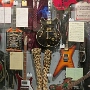 Links eine Doubleneck SG von Jimmy Page, daneben der Jack Daniel's Bass von Michael Anthony, ein Rickenbacker Bass von Cliff Burton, eine Lucille von B.B. King, eine Dean von Dimebag, ein bunter Bass und oben irgendetwas Rotes....
